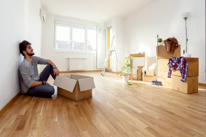 Happy young man just moved into new home unpacking boxes sitting on the floor